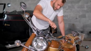 Orta yaşlı bir adam garajda retro motorsikletini tamir ediyor. Atölyede motosiklet tamir eden kendine güvenen genç adam..