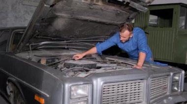 Bir araba tamircisi eski bir arabanın motorunu inceliyor. Eski arabaların tamiri.