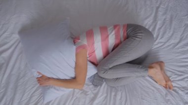 Genç bir kadın başını yastığın altına koyup yatağa uzanıyor. Depresyon ya da akıl sağlığı sorunları. Yatakta yatan, başını yastıkla saklayan, umutsuzluk hisseden genç bir kadının en iyi görüntüsü..
