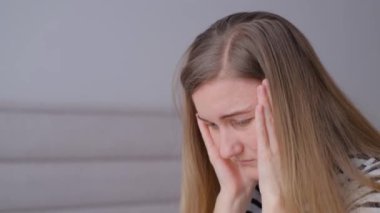 Şiddetli baş ağrısı olan bir kadın, el ele tutuşuyor. Kanepede oturan başı ağrıyan genç bir kadın. Üzgün, hayal kırıklığına uğramış, bir sorun için endişelenen, stresli bir kız.. 