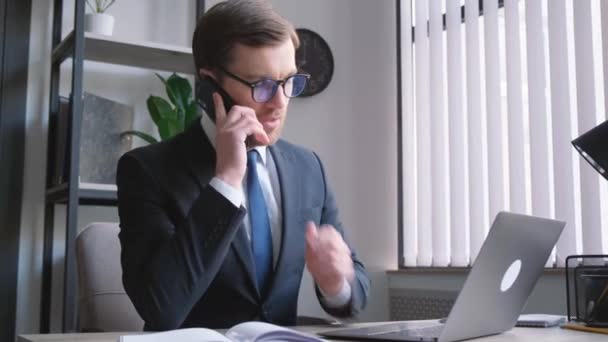 Biznesmen Okularach Rozmawia Przez Telefon Siedzi Przy Stole Laptopem Przyjazny — Wideo stockowe