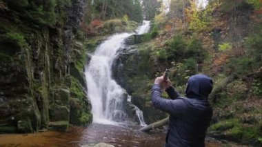 Bir erkek turist, şelalenin yakınındaki bir akıllı telefondan fotoğraf çekiyor. Tatil.