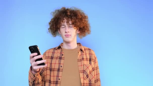 Curly Chlap Chytrým Telefonem Ruce Modrém Pozadí Studiu — Stock video