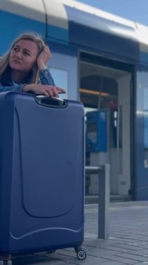 Bir kadın yolcu tren istasyonunda tren beklerken bir bavulun üzerinde uyur. Turizm kavramı. Dikey video