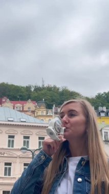 Bir kadın Karlovy Vary 'deki bir kaynaktan maden suyu içiyor. Turizm kavramı. Dikey video.