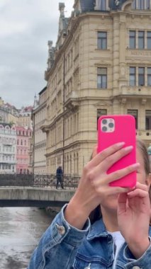 Güzel bir kız eski bir Avrupa şehrinin fotoğrafını çekmek için akıllı telefon kullanır. Seyahat konsepti. Dikey video.