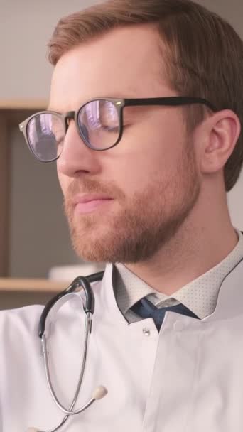 白いコートを着た若いインターン医師がカメラを見て微笑んでいる バーティカルビデオ — ストック動画