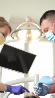 Modern bir klinikte dişçi ve asistan dişleri tedavi eder. Ağrısız diş tedavisi. Dikey video.