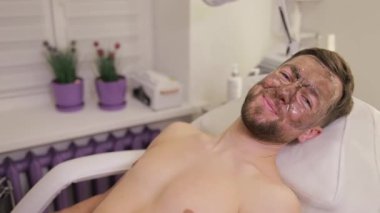 Siyah maske takan erkekler için spa terapisi. Genç bir adam güzellik salonunda maske takıyor.. 