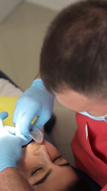 Genç bir erkek dişçi diş kliniğinde oral genişletici çekiyor. Diş hekimliğinde Cofferdam. Doktor koltuğunda oturan genç bir kadın dişlerini tedavi ediyor. Dişlerin temizlenmesi ve önlenmesi. Dikey video