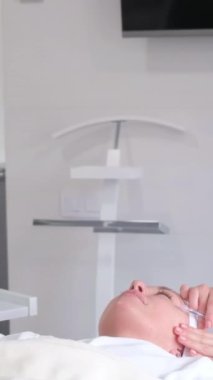 Bir güzellik uzmanı bir kadının yüzüne gençleştirici iğneler yapar. Dikey video.
