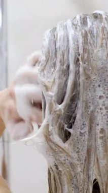 Seksi sarışın kadın, duşta başını yıkar. Genç bir kadın saçını yıkıyor ve duş alıyor. Saç bakımı. Dikey video