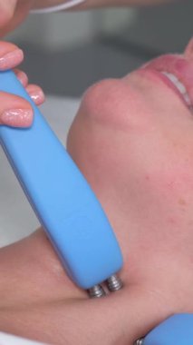 Elektriksel uyarımlı kadın yüz masajı. Cilt tazeleme. Güzellik salonu. Dikey video.