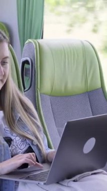 İş gezisinde olan genç bir iş kadını. Bilgisayarını kullanarak otobüste çalışıyor. Seyahat eden iş hayatı tarzı kadın insanlar. Dikey video.