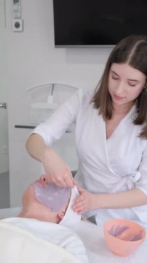 Dikey videoda, bir kozmetik uzmanı cilt bakımı sırasında nemlendirici bir maskeyle bir insanın derisini kaplar. Dikey video