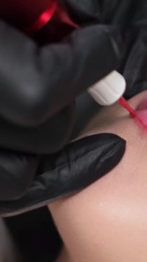 Salonda kalıcı olarak dudak makyajı yapılan genç bir kadın, yakın plan. Kozmetik uzmanı, kuafördeki müşteriye kalıcı makyaj prosedürünü uyguluyor. Dikey video