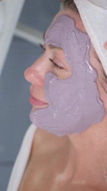 Profesyonel bir kozmetikçi cilt bakımı sırasında nemlendirici bir maskeyle bir insanın derisini kaplar. Dikey video