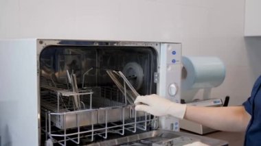 Bir tıp uzmanı içinde birkaç metal diş aleti olan bir otoklavı açıyor. Tıbbi aletlerin dezenfeksiyonu.