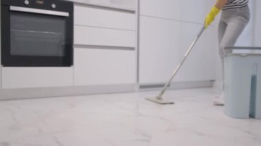 Hızlı ev işi yapan çalışkan bir kadın modern beyaz mutfak içinde mükemmel seramik zemin paspaslıyor..