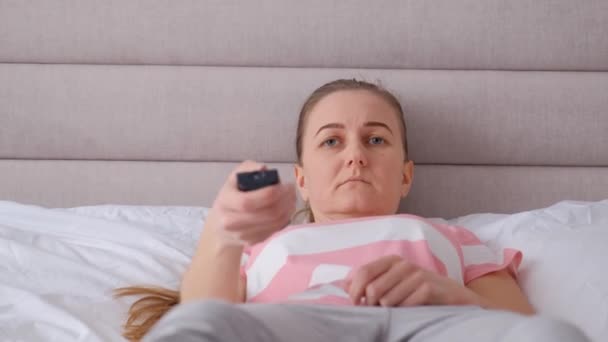 疲れた女性はベッドの上に横たわり テレビを見る — ストック動画