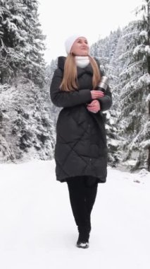Karlı bir ormanda yol boyunca yürüyen genç bir kadın. Kız karlı ormanda yürüyor ve doğaya hayran..