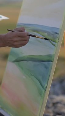 Ressam yağlı boyalarla bir resim çiziyor, yakın plan. Dikey video.