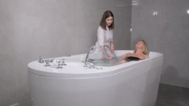 Bir kaplıca işçisi müşterisiyle jakuzide esnek bir tüpü suya indiriyor..