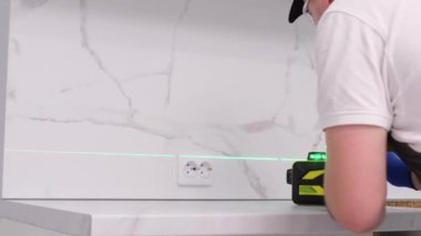 Üniformalı bir müteahhit, yeni bir dairede mobilya montajının kalitesini kontrol ediyor. İnşaat ve onarım kavramı. Elektronik inşaat lazeri kullanımı.