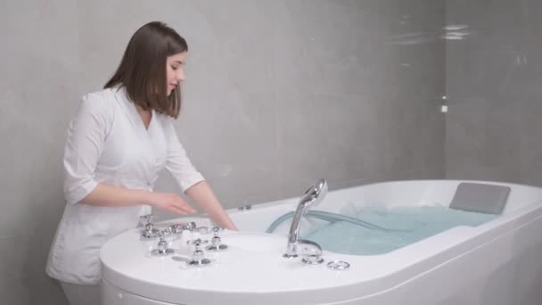 女性のスパの専門家は ハイドロマッサージ手順のための湯でバスタブを満たしています プロのハイドロマッサージ — ストック動画
