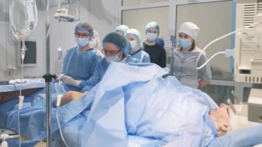 Bir doktor ve asistanlar yaşlı bir kadını ameliyat ediyorlar. Cerrahi operasyondaki öğrenciler.