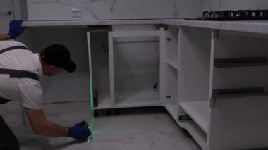 Gri tulumlu yetenekli bir zanaatkar inşaat lazeri kullanarak mobilya kuruyor..