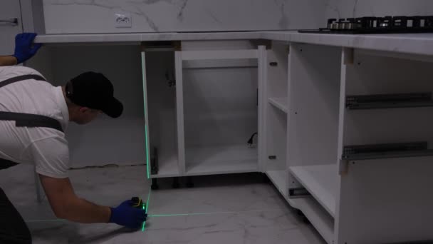 Wykwalifikowany Rzemieślnik Szarym Kombinezonie Instaluje Meble Pomocą Lasera Budowlanego — Wideo stockowe