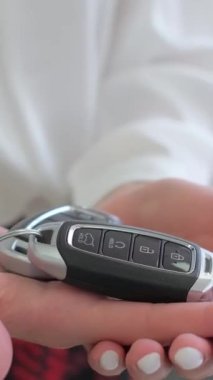 Yeni bir arabanın anahtarlarını tutan bir kadın elinin yakın çekimi. Bir kadın alıcı elektrikli bir araba satın alır. Dikey video.