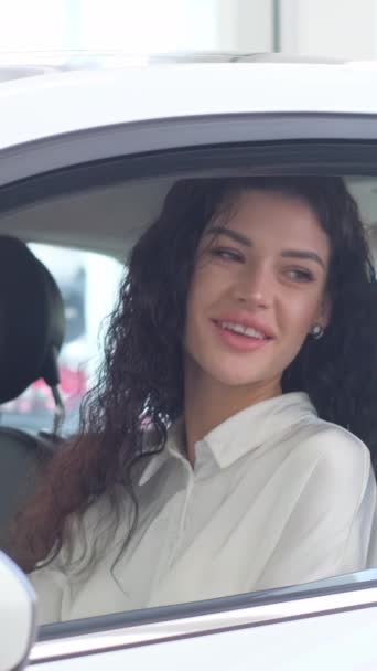 Portrait of a happy woman driving a new luxury electric car in a car showroom. A woman shows emotions of happiness in her new car. Vertical video.