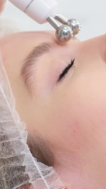 顔のマイクロカレントと呼ばれる刺激的な顔療法を行う美容師のクローズアップ 女性が直面する美容ケア バーティカルビデオ — ストック動画