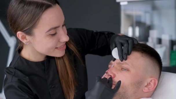 一个有魅力的男人在化妆品诊所接受鼻膜充填手术 一个穿着制服的女人在一家美容院打针 — 图库视频影像