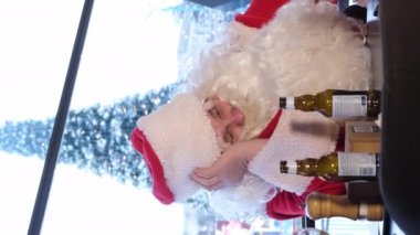 Pub 'daki komik sarhoş Noel Baba. Psikolojik olarak bitkin Noel Baba ve bir şişe bira. Mutlu noeller. Dikey video.