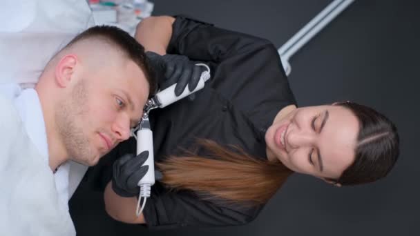 在垂直录像中 美容师正在用超声波洗掉年轻人脸上的粉刺和伤疤 — 图库视频影像