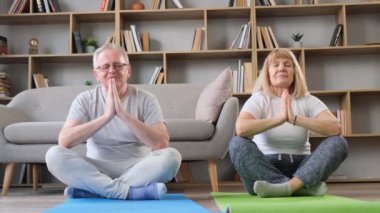 Aktif kıdemli çift evde vakit geçirirken yoga yapıyor ve gülümsüyor. Yaşlı çift evde birlikte rahatlama egzersizi yapıyor.. 