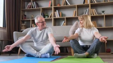 Mutlu sağlıklı 60 'lı yaşlarda bir çift eğleniyor, meditasyon yapmayı öğreniyorlar, evde spor egzersizleri yapıyorlar..