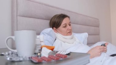 Grip olan bir kadın kendini cadı, ilaç, çay ve yatakta yatarak iyileştiriyor. Kadın hasta ve yorgun görünüyor..