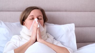 Genç bir kadın üşütmüş. Sağlık ve hasta insanlar kavramı. Genç bir kadın yatak odasında beyaz bir yatakta mendile hapşırıyor, grip ve alerji konsepti.. 