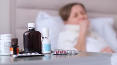  Ön planda, arka planda su toplayan bir çantadaki hap yatakta yatan bulanık bir genç kadının güçlü bir öksürüğü vardır. Sağlık ve ilaç kavramı.