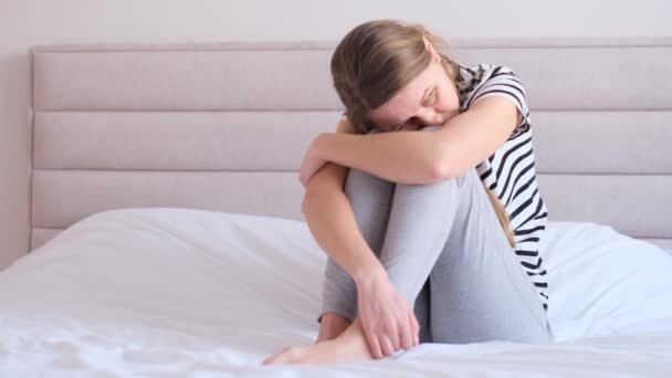 忧心忡忡的女孩一个人坐在床上 抱着自己 感到孤独 经历着心理问题的创伤 思考着卧室里的问题 — 图库视频影像