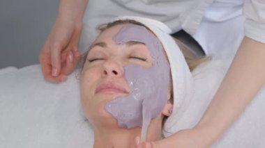  Bir kozmetolog, kozmetoloji kliniğindeki hastalara maske takar. Profesyonel yüz temizleme, deri soyma, kozmetoloji konsepti..