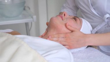 Güzel bir kadın yatakta uzanıyor, yüz masajı yapıyor sağlık spası, yaşlanma önleyici spa ve yüz bakımı uzmanı tarafından.. 