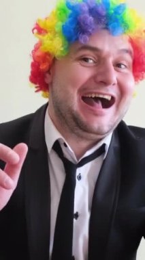 Renkli peruklu dans eden genç bir adam ellerini stüdyo arka planında ritmik olarak hareket ettiriyor. Dikey video.