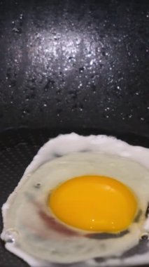 Tavada cızırdayan bir yumurtanın yakın çekimi, ağır çekimde çekilmiş. Yemek pişirme konsepti. Dikey video.