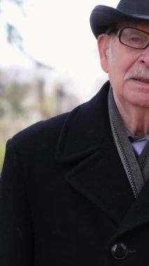 Son sınıf öğrencisi sonbahar parkında yürüyor, siyah bir ceket ve şapka giyiyor. Yaşlılar için sonbahar moda giysileri. Dikey video