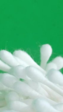 Beyaz renkli pamuklu çubuklar yeşil arka planda daire şeklinde döner. Hijyen ürünleri. Dikey video